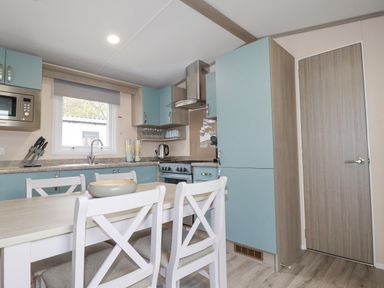 A kitchen with blue cabinets a dining table with chairs and a microwave at The Mermaid A04 in Par