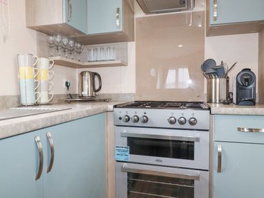 A kitchen corner with a stove kettle stacked mugs utensils and a coffee machine at The Mermaid A04 in Par