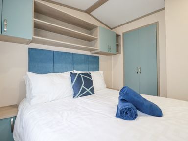 A bedroom with a blue headboard white bed linens two blue rolled towels and blue cabinets at The Mermaid A04 in Par