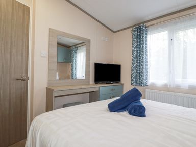 A bedroom with a bed with blue towels on it a dresser with a mirror and a television by the window at The Mermaid A04 in Par
