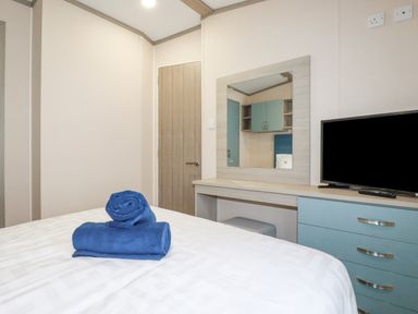 A bedroom with a bed with blue towels on it a wooden door a dresser with a mirror and a television at The Mermaid A04 in Par