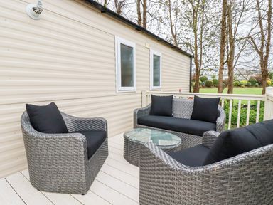 An outdoor seating area with a sofa two armchairs and a glass table on a deck at The Mermaid A04 in Par