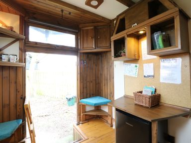 A wooden interior room with a small kitchenette, a fridge, shelves, a cork board with papers, and a door leading outside at Daisy Cow Shed 1 Easton near Campsea Ashe