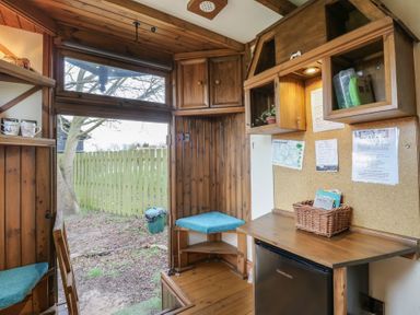 A small wooden room with a door opening to a fenced garden a mini fridge a wooden desk and cushioned corner seats at Daisy Cow Shed 1 Easton near Campsea Ashe