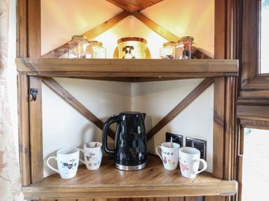A wooden kitchen shelf with a black electric kettle and four mugs near a window at Daisy Cow Shed 1 in Easton near Campsea Ashe