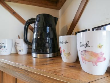 A wooden shelf with animal-themed mugs and a black textured kettle at Daisy Cow Shed 1 Easton near Campsea Ashe