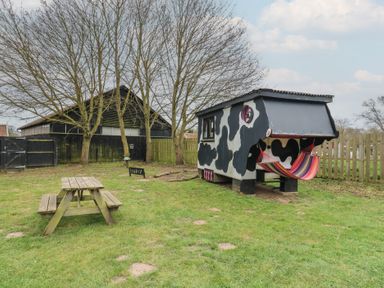 A yard with a wooden picnic table and a small cow-patterned shed with a hammock at Daisy Cow Shed 1 Easton near Campsea Ashe