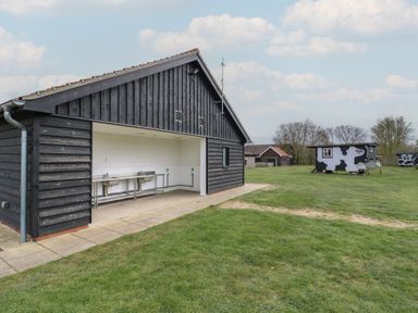 A black wooden shed with stainless steel sinks on a grassy field with cow-patterned huts at Daisy Cow Shed 1 in Easton near Campsea Ashe