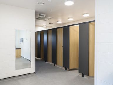 A row of bathroom stalls with wooden doors and black panels in a restroom with a mirror on the wall at Daisy Cow Shed 1 in Easton near Campsea Ashe