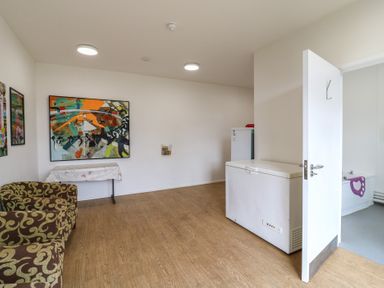 A room with patterned armchairs a table a freezer and an open door showing a bathroom at Daisy Cow Shed 1 Easton near Campsea Ashe
