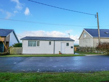 A small white house with a tiled roof and a front door beside a street at Ael Y Don in Llandanwg