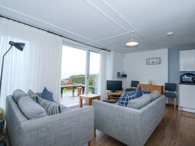 A living room with two grey sofas a small wooden coffee table a TV on a stand and sliding glass doors leading to a deck at Ael Y Don in Llandanwg