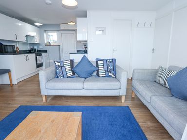 A living room with two sofas and a wooden coffee table next to an open kitchen at Ael Y Don in Llandanwg