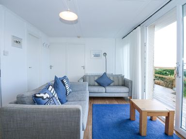 A living room with two gray sofas with blue cushions a wooden coffee table and a blue rug next to a glass sliding door at Ael Y Don in Llandanwg