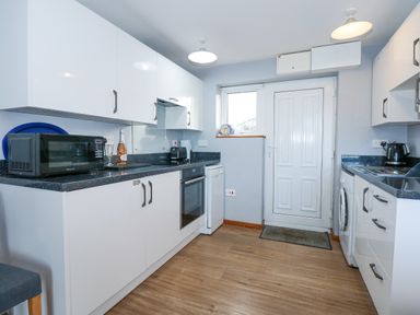 A kitchen with white cabinets black countertops a microwave oven dishwasher washing machine and a door at Ael Y Don in Llandanwg