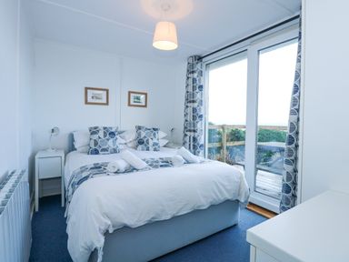 A bedroom with a double bed pillows bedside tables lamps glass doors and curtains at Ael Y Don in Llandanwg