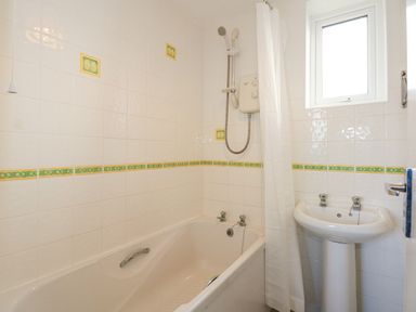 A bathroom with a bathtub shower combination a sink and a window at Ael Y Don in Llandanwg