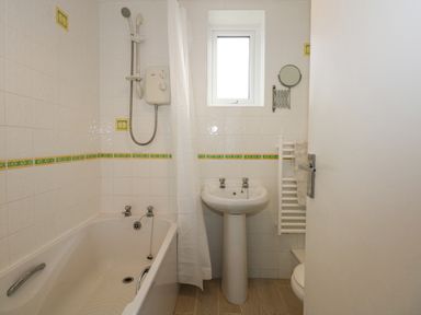 A bathroom with a bathtub shower curtain sink towel radiator and a small window at Ael Y Don in Llandanwg