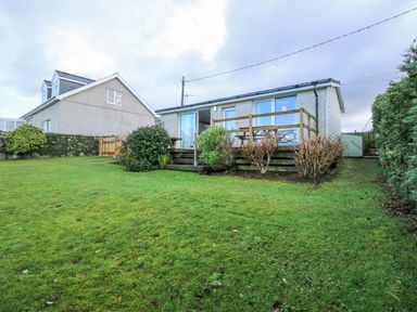 A single story house with a wooden deck and garden surrounded by bushes at Ael Y Don in Llandanwg