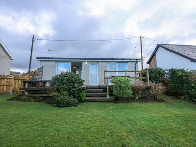 A single story house with wooden deck and shrubs in front at Ael Y Don in Llandanwg