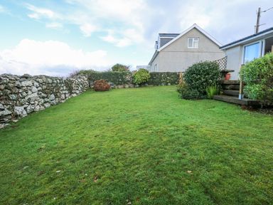 A garden with grass bushes and stone walls beside houses at Ael Y Don in Llandanwg