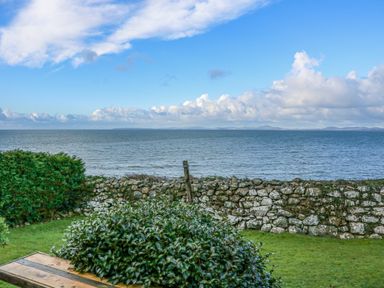 A view of the sea with clouds a stone wall bushes and grass at Ael Y Don in Llandanwg