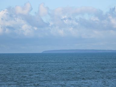 A view of the sea with a distant coastline and cloudy sky at Ael Y Don in Llandanwg
