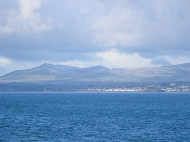 A coastal view with a body of water in the foreground and hills and buildings in the background at Ael Y Don in Llandanwg