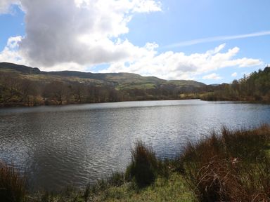 A lake with hills and trees in the background at Ael Y Don in Llandanwg