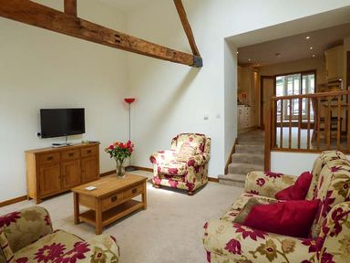 A living room with floral armchairs a wooden TV stand with a television a wooden coffee table and a floor lamp at Ghyll Bank Barn in Staveley near Windermere