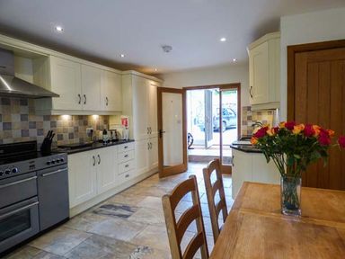 A kitchen with cream cabinets a dining table with chairs and flowers on the table at Ghyll Bank Barn in Staveley near Windermere