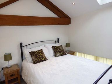 A bedroom with a double bed with white linens and floral pillows with wooden beams and wooden bedside tables with lamps at Ghyll Bank Barn in Staveley near Windermere