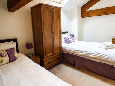 A bedroom with two single beds a wooden wardrobe bedside tables and exposed wooden beams at Ghyll Bank Barn in Staveley near Windermere