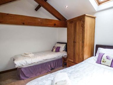 A bedroom with two single beds wooden wardrobe and exposed ceiling beams at Ghyll Bank Barn in Staveley near Windermere