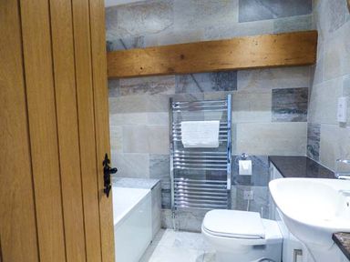 A bathroom with a wooden door a bathtub a heated towel rail a toilet and a sink at Ghyll Bank Barn in Staveley near Windermere