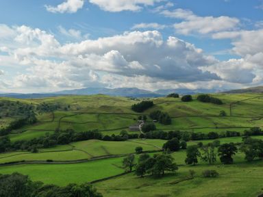 Green fields with trees and stone fences under a cloudy sky at Ghyll Bank Barn in Staveley near Windermere
