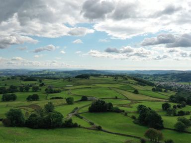 A green rural landscape with trees sheep and fields separated by stone walls under a cloudy sky at Ghyll Bank Barn in Staveley near Windermere