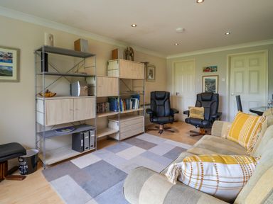 A living room with black armchairs a beige sofa with cushions shelves with books and decor at 50 Fernhill Heights in Charmouth