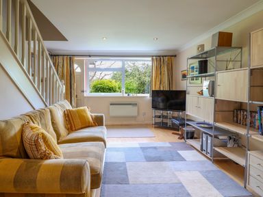 A living room with a striped sofa cushions a window with curtains a television and shelving unit at 50 Fernhill Heights in Charmouth
