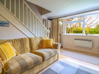 A living room with a striped sofa and yellow cushions near a staircase and window at 50 Fernhill Heights in Charmouth