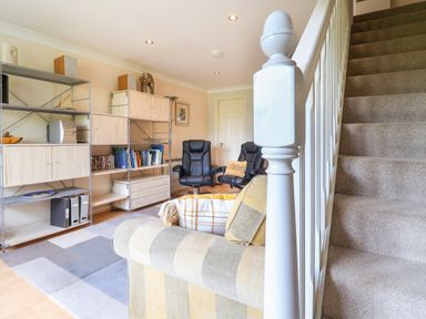 A living room with a striped sofa two black chairs a shelving unit and carpeted stairs at 50 Fernhill Heights in Charmouth