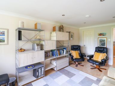 A living room with black armchairs yellow pillows shelving units and framed pictures at 50 Fernhill Heights in Charmouth