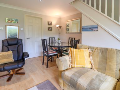 A living room with a beige striped sofa and yellow cushion a black leather armchair a round glass dining table with four chairs and wall art at 50 Fernhill Heights in Charmouth