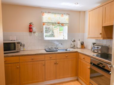 A kitchen with wooden cabinets a microwave a sink a toaster a knife block and an oven at 50 Fernhill Heights Charmouth