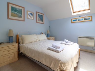 A bedroom with a bed featuring white bedding and folded towels on top with nightstands and lamps on each side at 50 Fernhill Heights in Charmouth