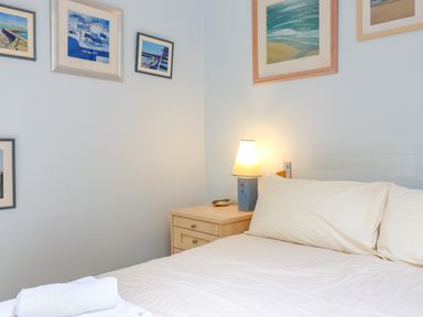 A bedroom with a bed pillow and white linens next to a wooden nightstand with a lamp and framed artwork on the walls at 50 Fernhill Heights in Charmouth