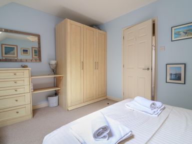 A bedroom with a bed and towels a wardrobe a chest of drawers and framed pictures on the wall at 50 Fernhill Heights in Charmouth