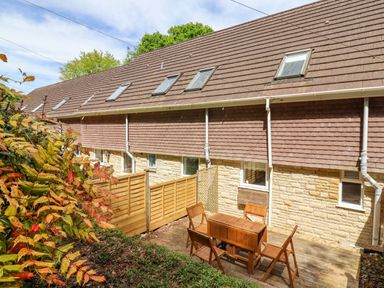 An outdoor patio area with wooden table and chairs next to a residential building with brown roof tiles and light stone walls at 50 Fernhill Heights in Charmouth