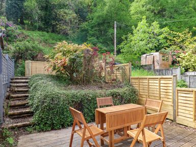 A garden with wooden patio furniture a wooden deck and a staircase leading to a grassy hill at 50 Fernhill Heights in Charmouth