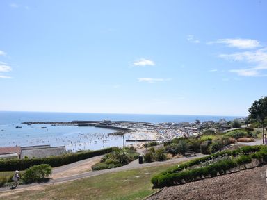 A coastal view with a beach full of people, a harbor, and pathways with greenery overlooking the sea at 50 Fernhill Heights in Charmouth